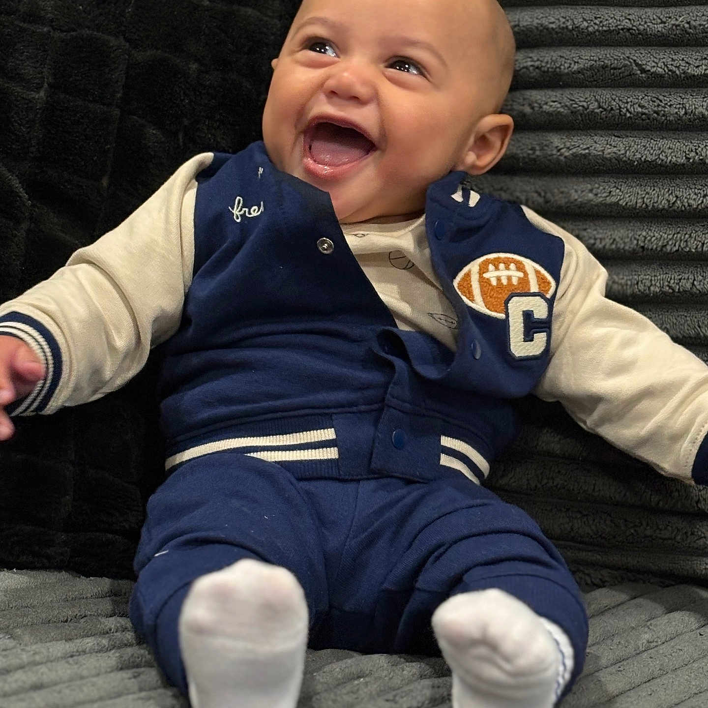 Phinesse is registered to the contest to win money with this photo: baby, blue_jacket, child, clothing, comfort, couch, cozy, cute, expression, face, happy, indoor, infant, laughing, plush, portrait, seated, smiling, soft_texture, white_socks