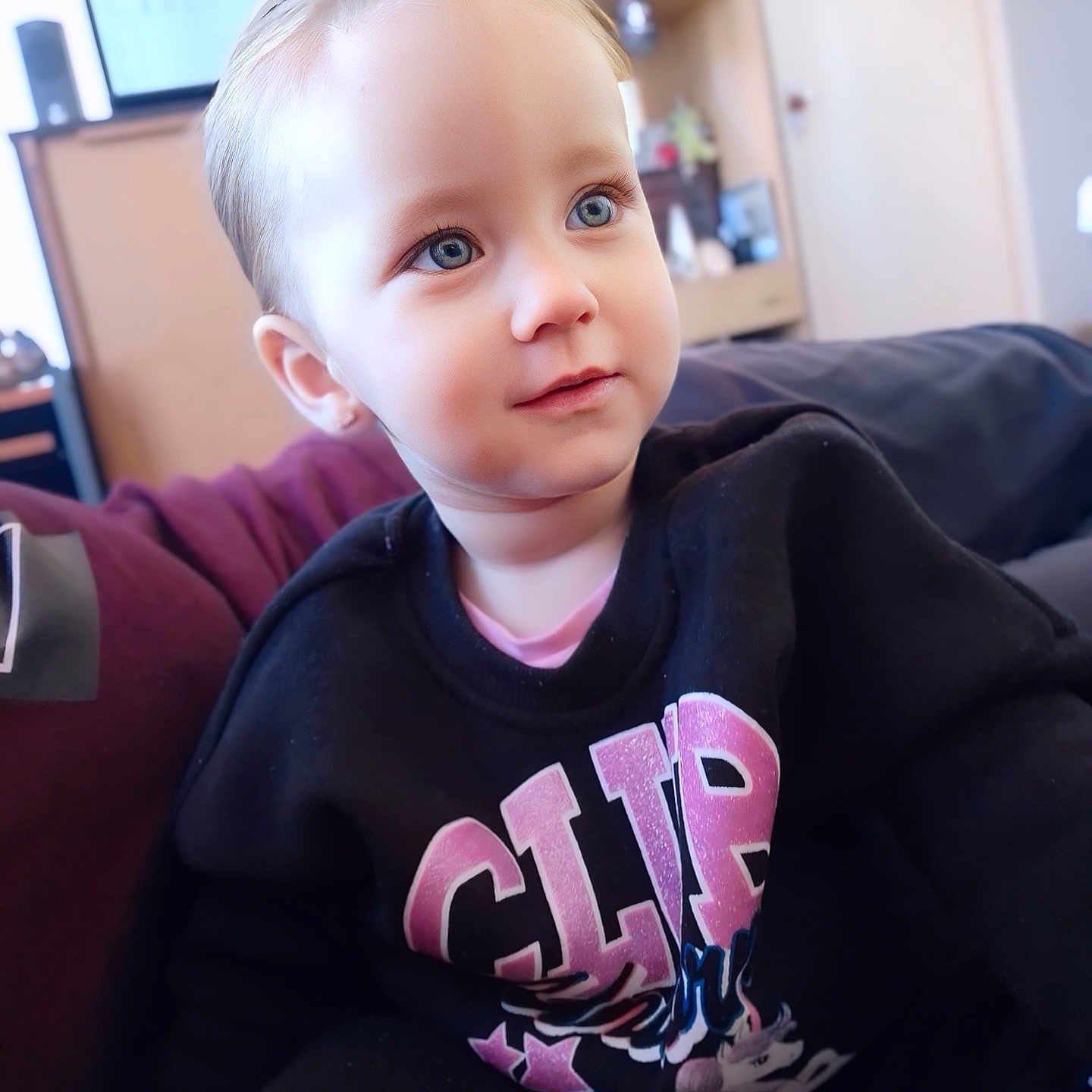 Lyrah is registered to the contest to win money with this photo: black_sweatshirt, blue_eyes, bright, casual_clothing, child, couch, cozy, cute, face, furniture, hair, home, indoor, person, portrait, relaxed, sitting, smiling, toddler, young_child