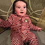 baby, checkered, child, clothing, couch, curious, face, happy, head, indoor, infant, pajamas, patterned, person, red, seated, smiling, sofa, white, young