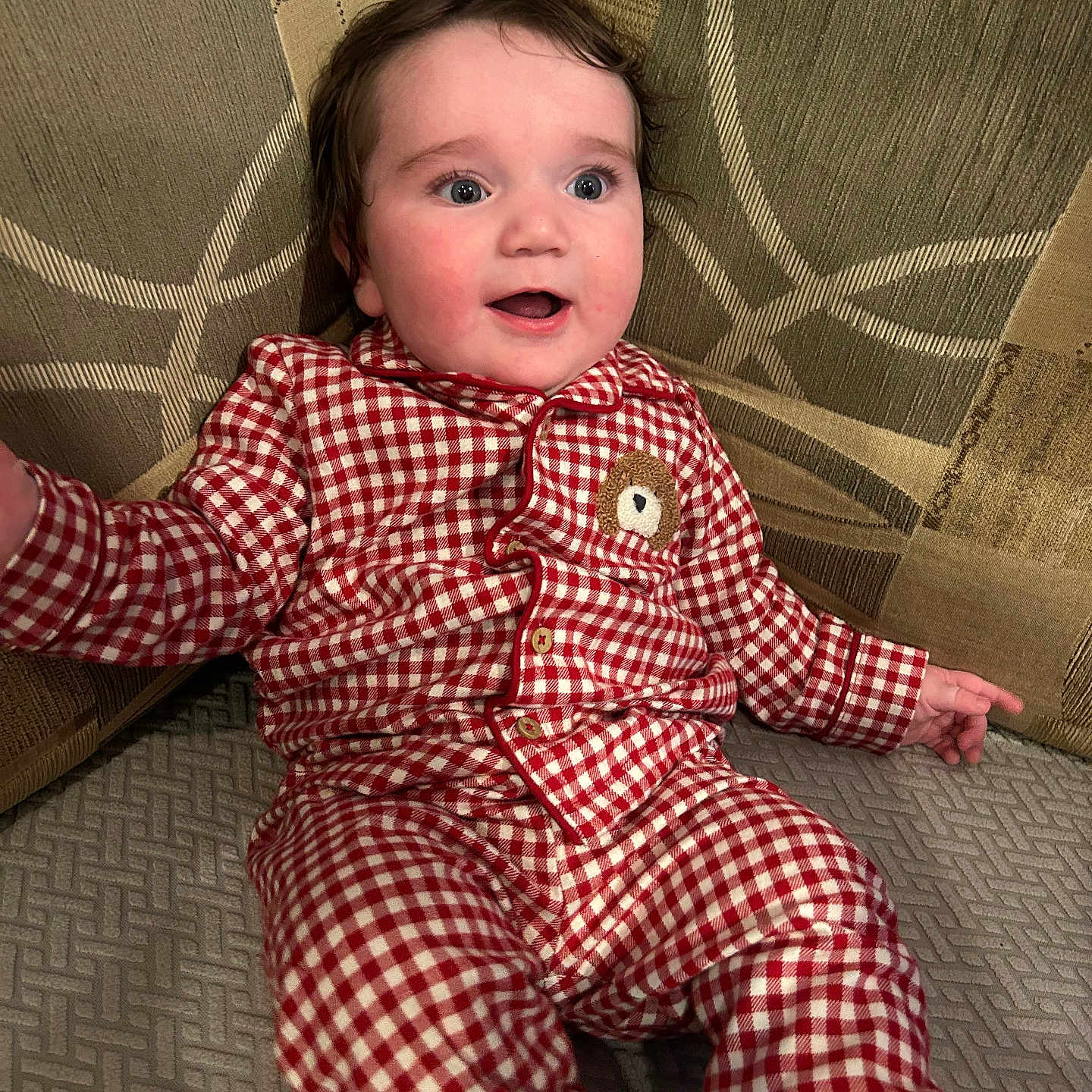 Ellis is registered to the contest to win money with this photo: baby, checkered, child, clothing, couch, curious, face, happy, head, indoor, infant, pajamas, patterned, person, red, seated, smiling, sofa, white, young