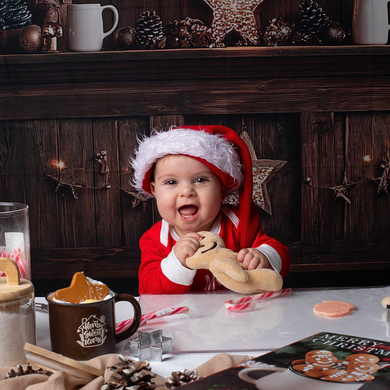 Eléa participe au concours pour gagner de l'argent avec cette photo : baby, candy_cane, child, christmas_book, christmas_theme, cookie_cutter, cute, festive, gingerbread_plush, happy, holiday_decor, indoors, mug, pinecones, red_clothing, santa_hat, smiling, table, toy, wooden_background