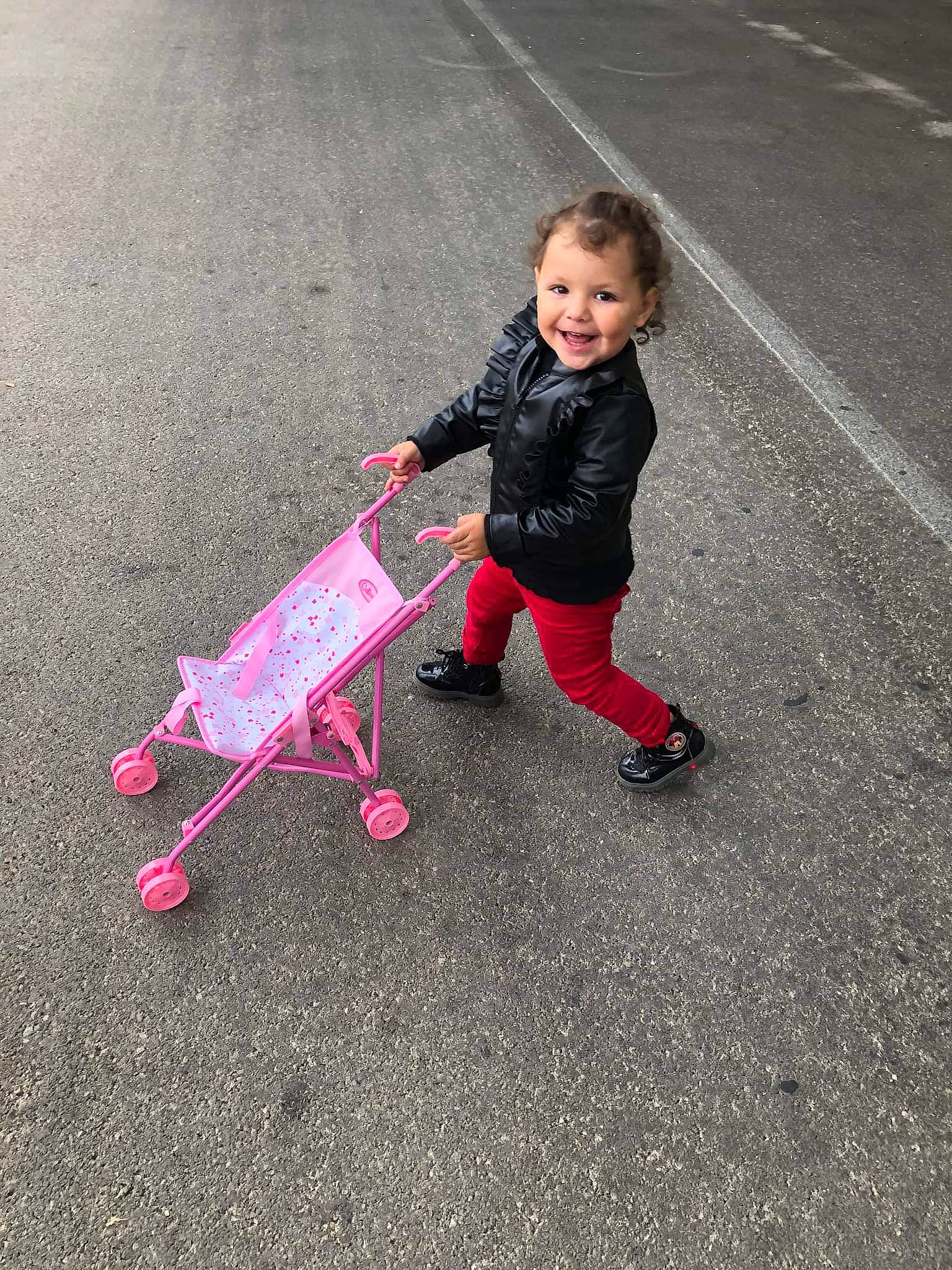 Noëlia a rejoint le concours — aidez-le/la à gagner de superbes lots ! asphalt, automotive_wheel_system, baby_carriage, baby_products, child, fun, joy, leisure, magenta, people_in_nature, person, play, recreation, road, road_surface, rolling, sidewalk, sitting, smile, tire