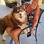 Rusty is registered to the contest to win money with this photo: woman, dog, husky, pet, smiling, tattoos, chair, phone, outdoor, porch, casual, happy, fur, blue_eyes, sneakers, tank_top, summer, grill, storage_boxes, companionship