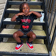 Nalonie is registered to the contest to win money with this photo: child, stairs, outdoor, black_tshirt, red_shoes, bracelet, necklace, pose, metal_stairs, concrete, sidewalk, cup, tumbler, hair, person, fashion, casual, smiling, young, sitting