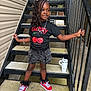 child, girl, smiling, stairs, outdoor, black_tshirt, red_sneakers, shorts, bracelet, necklace, railing, metal_stairs, curly_hair, white_tumbler, casual_clothing, fashion, young, playful, standing, daylight