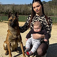 Rex participe au concours pour gagner de l'argent avec cette photo : woman, baby, dog, outdoor, sunlight, grass, gravel, nature, portrait, casual_clothing, long_hair, sitting, kneeling, puppy, pet, animal, child, young_adult, fence, trees