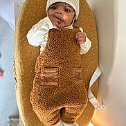 Arlo joined the competition — help win amazing prizes! baby, infant, child, hat, knitted_hat, ears, overalls, brown_overalls, white_shirt, cushioned_pad, mustard_yellow, changing_pad, hand_in_mouth, curious_expression, indoor, soft_lighting, white_wall, baby_clothing, footwear, toddler