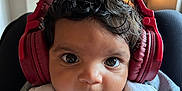 Arlo is registered to the contest to win money with this photo: baby, child, headphones, bib, indoor, portrait, cute, face, curly_hair, smile, person, clothing, closeup, expression, young, infant, indoors, cozy, looking_at_camera, adorable