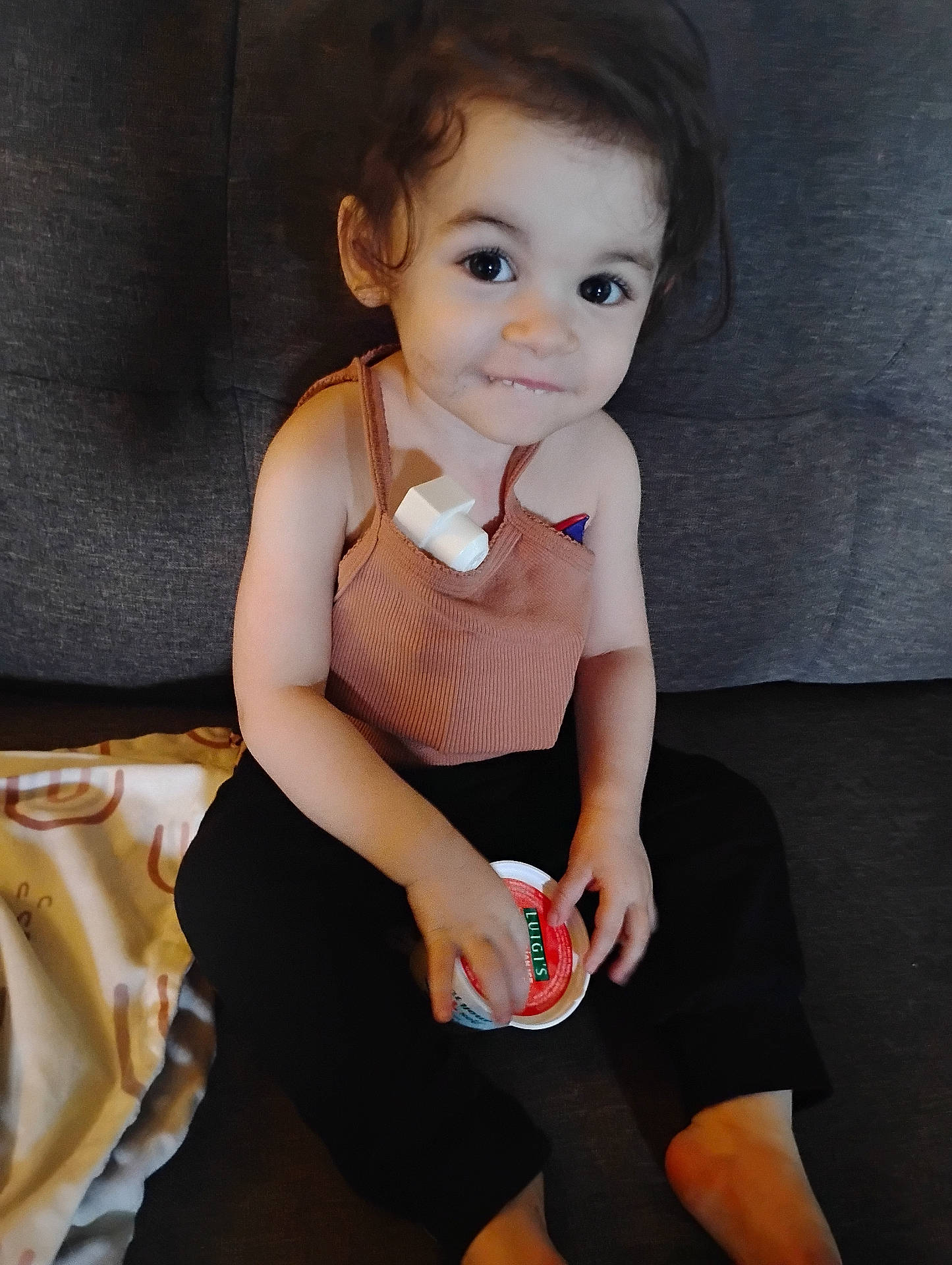 Ophelia is registered to the contest to win money with this photo: barefoot, blanket, child, clothing, container, couch, curly_hair, cute, face, hand, home, indoor, person, playful, sitting, skin, smile, tank_top, toddler, young_child