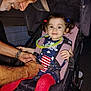 child, toddler, stroller, man, tattoo, seatbelt, red_tights, hair_ties, american_flag, night, outdoor, smile, curly_hair, protective, clothing, hands, face, person, transportation, family