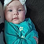 baby, child, infant, blue_eyes, headband, white_bow, teal_clothing, floral_print, close_up, portrait, cute, soft_skin, indoor, comfort, young, small_hands, expression, face, person, newborn