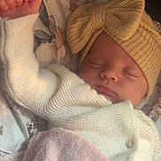 Swaïly participe au concours pour gagner de l'argent avec cette photo : baby, infant, newborn, sleeping, hat, knit_hat, bow, blanket, swaddle, cozy, peaceful, portrait, close_up, hand, fist, pink_blanket, white_cardigan, button, floral_bedding, sleepy_face