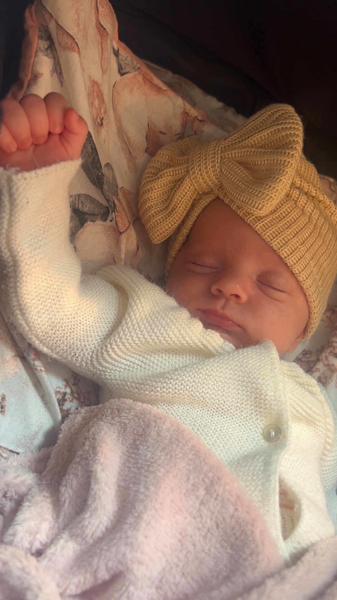 Swaïly participe au concours pour gagner de l'argent avec cette photo : baby, infant, newborn, sleeping, hat, knit_hat, bow, blanket, swaddle, cozy, peaceful, portrait, close_up, hand, fist, pink_blanket, white_cardigan, button, floral_bedding, sleepy_face