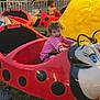 child, toddler, carnival, ride, ladybug, pink_clothing, outdoor, festival, evening, tent, grass, fun, amusement_park, play, smile, curly_hair, seat, toy, entertainment, family