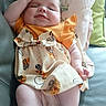 baby, infant, child, dress, couch, pillow, hand, face, smile, relaxed, indoors, skin, legs, sleeveless, patterned_clothing, cute, comfort, seated, young, happy
