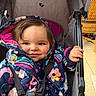Elsie joined the competition — help win amazing prizes! baby, child, stroller, jacket, colorful_clothing, smile, face, hand, seatbelt, fabric, indoor, person, cute, warm_clothing, patterned, holding, portrait, happy, young_child, cozy