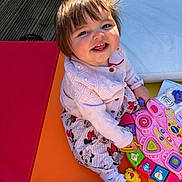 Elsie is registered to the contest to win money with this photo: toddler, child, smiling, toy, pink_toy, colorful, playtime, happy, cute, indoors, sitting, clothing, cardigan, patterned_pants, barefoot, sunlight, flooring, playmat, person, portrait
