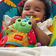 Meilani joined the competition — help win amazing prizes! baby, child, plush_toy, frog_toy, blanket, baby_seat, smiling, indoors, curly_hair, person, toy, couch, robotic_vacuum, colorful, white_clothing, soft_texture, comfort, happy, infant, playtime