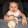 baby, child, high_chair, sippy_cup, bib, smiling, happy, pigtails, pink_clothing, hand, face, indoor, young_child, feeding_time, cute, cheerful, infant, table, playful, portrait