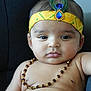 baby, child, face, headband, peacock_feather, necklace, yellow_clothing, bare_chest, infant, portrait, cute, indoor, sitting, closeup, expression, skin, jewelry, person, young, adorable
