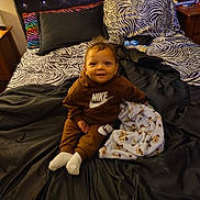 Zaiden joined the competition — help win amazing prizes! toddler, child, bed, blanket, pillow, clothing, nike, zebra_pattern, bedroom, smile, sitting, soft_toy, furniture, fabric, headboard, person, cozy, indoors, happy, casual_wear