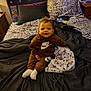 toddler, child, bed, blanket, pillow, clothing, nike, zebra_pattern, bedroom, smile, sitting, soft_toy, furniture, fabric, headboard, person, cozy, indoors, happy, casual_wear