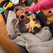 Chozien joined the competition — help win amazing prizes! baby, infant, car_seat, blanket, plush_toy, giraffe_toy, sunglasses, child, hand, wooden_floor, pink_sleeve, indoor, cozy, cute, striped_clothing, person, toy, soft_texture, colorful, casual