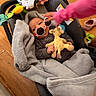 baby, infant, car_seat, blanket, plush_toy, giraffe_toy, sunglasses, child, hand, wooden_floor, pink_sleeve, indoor, cozy, cute, striped_clothing, person, toy, soft_texture, colorful, casual