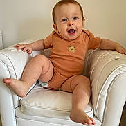 Sylvia Maria a rejoint le concours — aidez-le/la à gagner de superbes lots ! baby, casual_clothing, child, cute, floor_tiles, furniture, happy, home, indoor, infant, kicking_leg, leather_chair, lion_emblem, onesie, person, playful, seated, smiling, white_chair, young_child