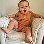 baby, casual_clothing, child, cute, floor_tiles, furniture, happy, home, indoor, infant, kicking_leg, leather_chair, lion_emblem, onesie, person, playful, seated, smiling, white_chair, young_child
