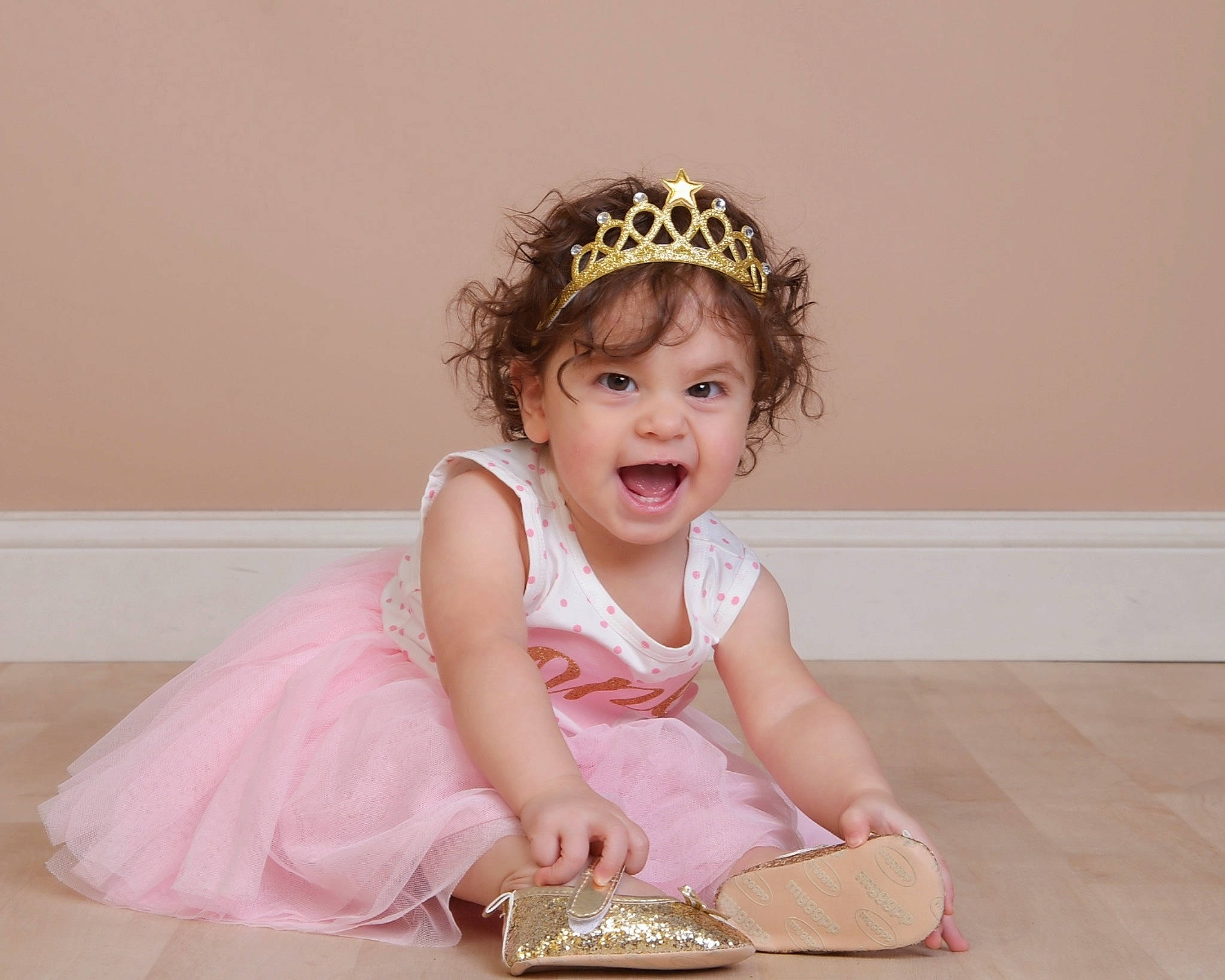 Meilani joined the competition — help win amazing prizes! baby_toddler_clothing, beige, child, child_model, costume_accessory, crown, dress, fashion_accessory, floor, hair_accessory, headband, headgear, headpiece, mouth, person, pink, sandal, sitting, tan, tiara