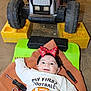 Raylynn is registered to the contest to win money with this photo: baby, infant, smiling, headband, red_bow, tools, screwdriver, wrench, toy_tractor, floor, clothing, long_sleeve, green_cushion, brown_cloth, indoor, child, happy, cute, playtime, football_theme