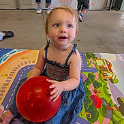 Gemma joined the competition — help win amazing prizes! background_people, blue_dress, casual, child, colorful, concrete_floor, curly_hair, feet, floor, indoor, legs, person, play_mat, playtime, red_ball, sitting, smiling, toddler, toy, young_child
