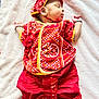 baby, sleeping, red_clothing, traditional_clothing, headwear, blanket, infant, cute, child, soft_texture, indoors, resting, peaceful, small_hands, footwear, patterned_fabric, portrait, cultural, newborn, lying_down