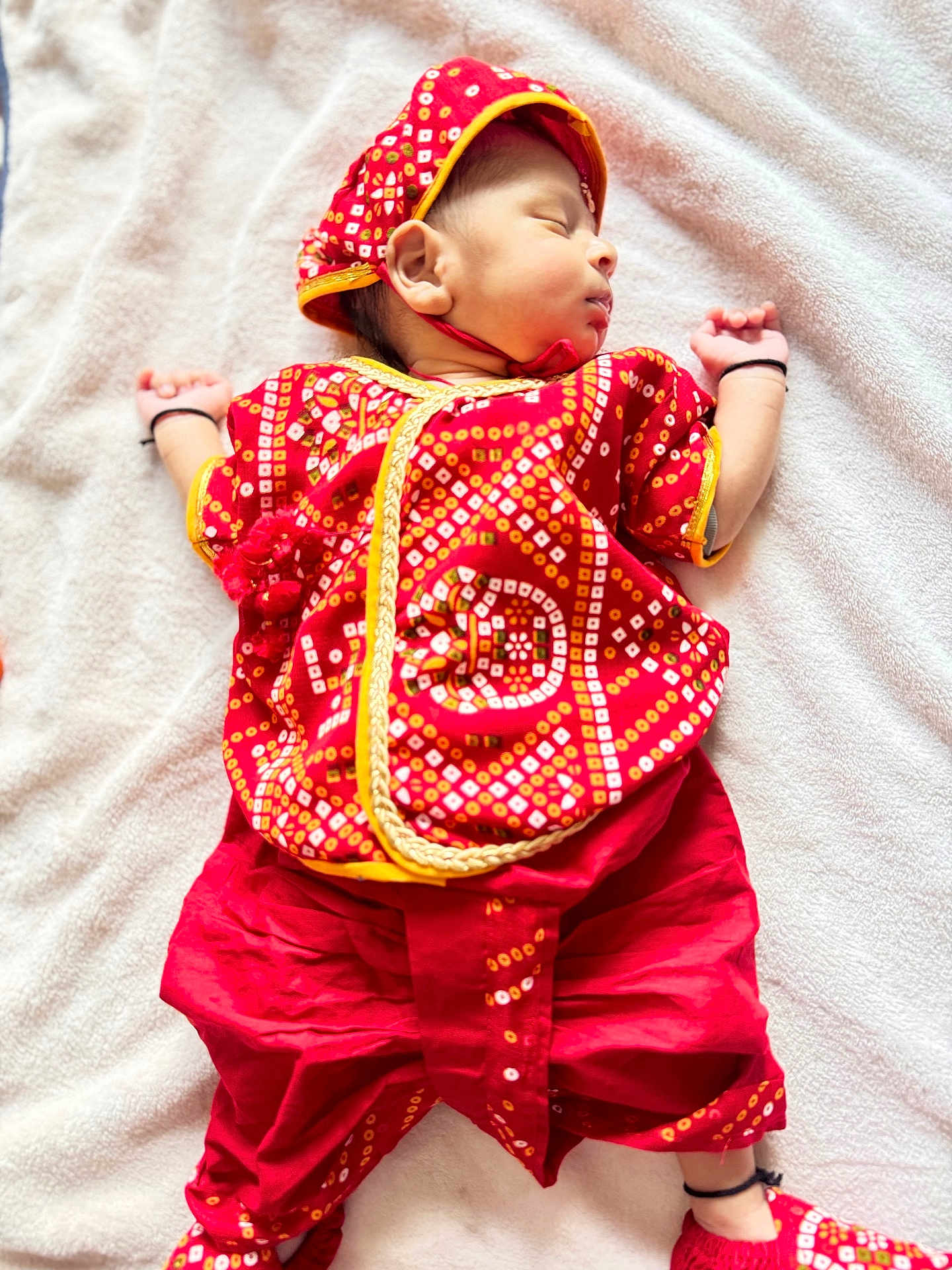 Leyan participe au concours pour gagner de l'argent avec cette photo : baby, sleeping, red_clothing, traditional_clothing, headwear, blanket, infant, cute, child, soft_texture, indoors, resting, peaceful, small_hands, footwear, patterned_fabric, portrait, cultural, newborn, lying_down