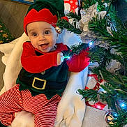 Roman is registered to the contest to win money with this photo: baby, child, christmas_elf_costume, christmas_tree, holiday, festive, gift_wrap, smiling, indoor, toy, decorations, red_and_green, striped_pants, hat, blanket, floor, face, joyful, holiday_season, celebration