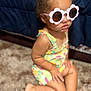 Rayanna is registered to the contest to win money with this photo: toddler, child, sunglasses, pink, flower_shaped, colorful_clothing, romper, carpet, indoor, cute, fashion, hair_ties, braided_hair, skin, barefoot, seated, portrait, closeup, baby, casual