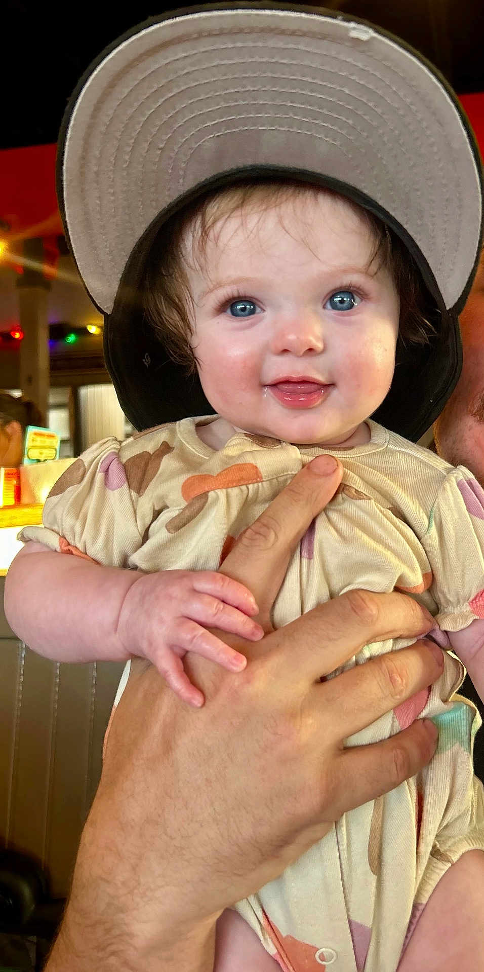 Elizabeth joined the competition — help win amazing prizes! baby, child, blue_eyes, cap, hat, smiling, hand, adult_hand, indoor, colorful_lights, face, cute, patterned_clothing, short_sleeves, infant, person, closeup, happy, skin, portrait