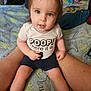 toddler, child, baby, person, sitting, legs, shirt, text, blue_eyes, blanket, dinosaur_pattern, clothing, indoor, cute, face, smile, shorts, skin, hair, home