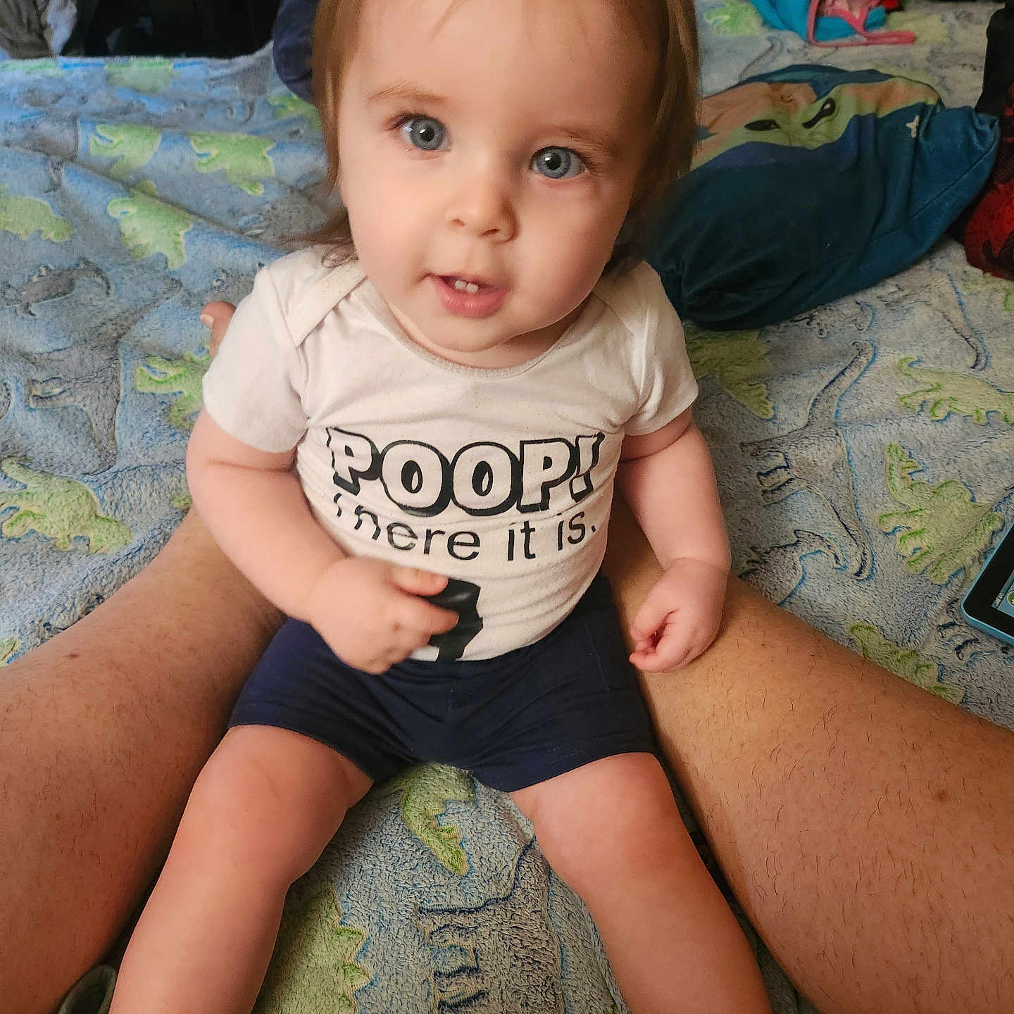 Kenneth joined the competition — help win amazing prizes! baby, blanket, blue_eyes, child, clothing, cute, dinosaur_pattern, face, hair, home, indoor, legs, person, shirt, shorts, sitting, skin, smile, text, toddler