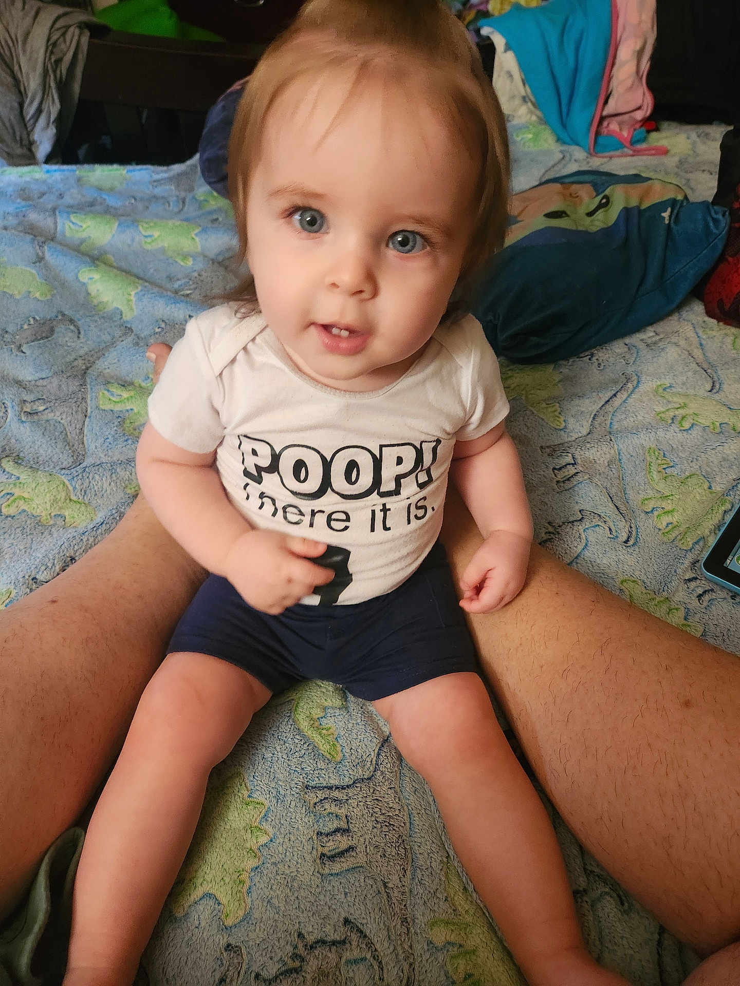 Kenneth joined the competition — help win amazing prizes! toddler, child, baby, person, sitting, legs, shirt, text, blue_eyes, blanket, dinosaur_pattern, clothing, indoor, cute, face, smile, shorts, skin, hair, home
