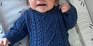 Reginald is registered to the contest to win money with this photo: baby, child, smiling, blue_sweater, green_pants, lying_down, changing_pad, sheep_pattern, infant, happy, cute, portrait, indoors, knitwear, young_child, person, baby_clothes, face, funny_expression, cozy