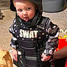 toddler, child, costume, swat, helmet, playful, tongue_out, indoors, carpet, camouflage, vest, toy_walkie_talkie, person, cute, funny_face, small_child, sitting, floor, home, pretend_play