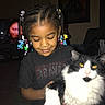 Sebastian joined the competition — help win amazing prizes! child, cat, indoor, hair_beads, black_and_white_cat, yellow_eyes, smiling, tshirt, carpet, television, furniture, dark_room, portrait, holding, pet, cute, home, person, animal, cozy