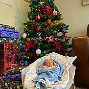 Jaxon joined the competition — help win amazing prizes! baby, sleeping, blanket, baby_rocker, christmas_tree, ornaments, presents, wrapped_gifts, holiday_decor, living_room, carpet, couch, festive_lights, indoors, cozy, infant, peaceful, red, green, blue