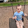 child, boy, swing, playground, chains, shorts, tshirt, smiling, outdoor, park, fence, tree, grass, skatepark, woodchips, footwear, happy, summer, recreation, casual