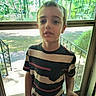 Theodore joined the competition — help win amazing prizes! child, boy, standing, striped_shirt, door, screen_door, window, glass, indoor, outdoor, trees, greenery, daylight, portrait, casual_clothing, person, young, natural_light, expressionless, background