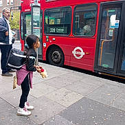 Victoria Opingo Calsas is registered to the contest to win money with this photo: backpack, bus_stop, casual_clothing, child, city, daytime, girl, outdoor, pavement, people, person, public_transport, red_bus, sidewalk, street, teddy_bear, transportation, urban, vehicle, waiting