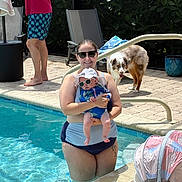 Savannah is registered to the contest to win money with this photo: woman, baby, swimming_pool, sunglasses, dog, man, towel, swimsuit, sunhat, poolside, outdoor, summer, family, water, greenery, baby_seat, paved_floor, pet, sunny, relaxation
