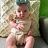 baby, infant, child, knitted_outfit, headband, bow, couch, pillow, cream_color, green_background, sitting, cute, portrait, indoor, soft_lighting, curious_expression, human, furniture, textile, closeup